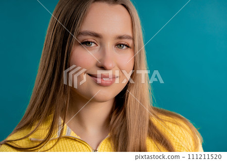 Young pretty woman in yellow sweater looking to camera on blue background. Face. Young pretty woman in yellow sweater looking to camera on blue background. Face. 111211520
