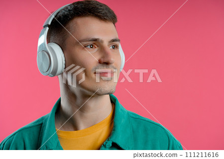Positive man listening music, enjoying dance with headphones on pink studio  111211616