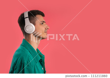 Positive man listening music, enjoying dance with headphones on pink studio  111211860