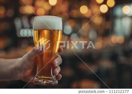 A hand holding big glass of foamy beer against blurred bar interior background with space for text A hand holding big glass of foamy beer against blurred bar interior background with space for text 111212277