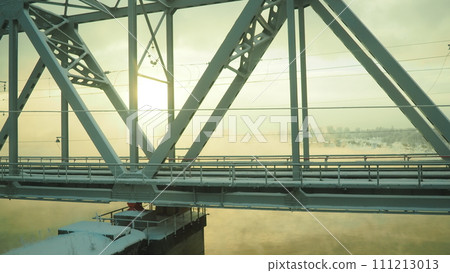 Volkhov, Russia, the railway bridge over the Volkhov River next to the hydroelectric power station. Severe frost -30 degrees Celsius. Low polar sun. Yellow cold fog. Volkhov, Russia, the railway bridge over the Volkhov River next to the hydroelectric power station. Severe frost -30 degrees Celsius. Low polar sun. Yellow cold fog. 111213013