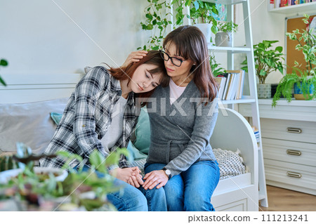 Upset sad hugged mother and daughter teenager sitting together on couch at home Upset sad hugged mother and daughter teenager sitting together on couch at home 111213241