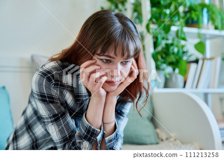 Upset sad young female sitting on couch at home 111213258