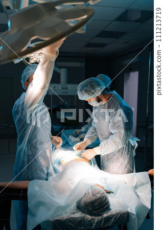 Vertical shot of being operated by professional surgeons. Male doctor adjusting light performing operation wearing medical gown. Surgeon adjusting surgical lamp before operation. Concept of emergency. Vertical shot of being operated by professional surgeons. Male doctor adjusting light performing operation wearing medical gown. Surgeon adjusting surgical lamp before operation. Concept of emergency. 111213719
