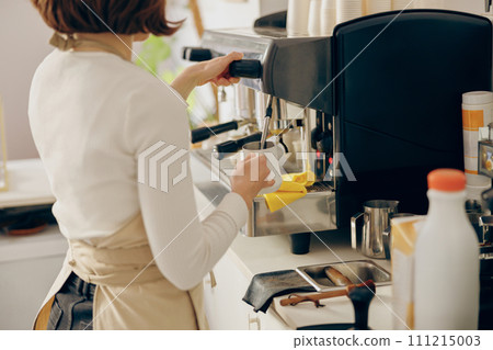 Close up of female barista froths milk on a coffee machine for making cappuccino or latte Close up of female barista froths milk on a coffee machine for making cappuccino or latte 111215003