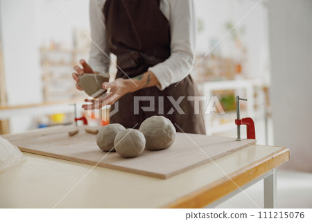 Close up of ceramist woman wearing apron is preparing clay to make pottery pieces in her studio Close up of ceramist woman wearing apron is preparing clay to make pottery pieces in her studio 111215076