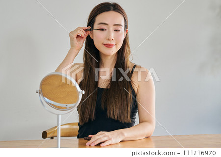 A woman in her 30s with long hair applying mascara 111216970