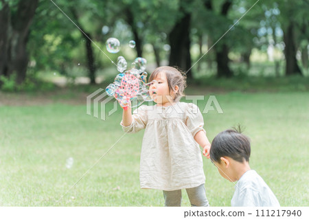 Siblings and children playing with soap bubbles in the forest/park (picnic/camping/outdoors) 111217940