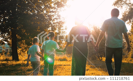 Mother and father with sons stroll hand in hand across meadow during family weekend 111218761