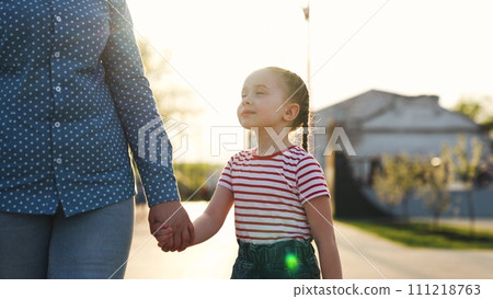 Unrecognizable mother walking with cute little baby daughter at sunny public park holding hands Unrecognizable mother walking with cute little baby daughter at sunny public park holding hands 111218763