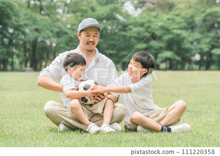 Brother and father playing with a soccer ball in a fresh green park (Family, Camping, Outdoors) 111220358