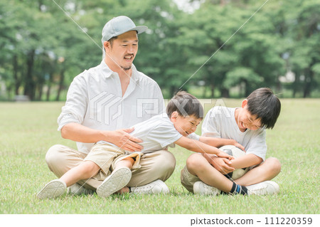 Brother and father playing with a soccer ball in a fresh green park (Family, Camping, Outdoors) 111220359