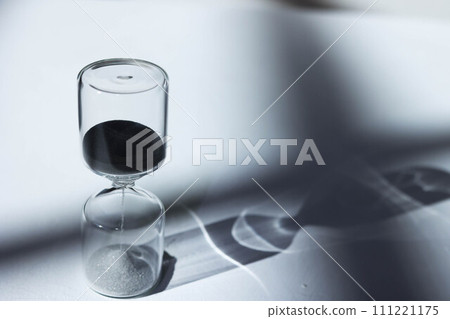 Hourglass on the desk, impressive light, shadow, and glass reflection Hourglass on the desk, impressive light, shadow, and glass reflection 111221175
