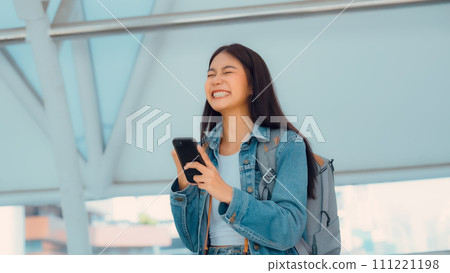 Happy female tourist wearing jeans jacket and holding smartphone at public Happy female tourist wearing jeans jacket and holding smartphone at public 111221198
