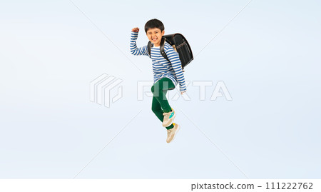 Elementary school boy jumping with a smile while carrying a school bag on his back 111222762
