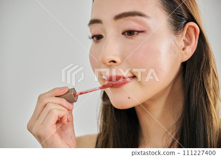 A woman in her 30s with long hair applying lip gloss 111227400