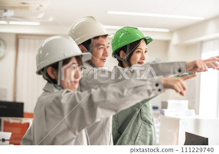 三名戴著頭盔的男女工程師互相指指點點 三名戴著頭盔的男女工程師互相指指點點 111229740