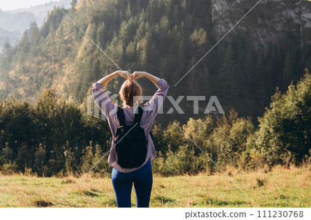 Freedom and active lifestyle concept. Adventure women making by hands in shape of love heart. Back view of Woman in active trekking clothes having a halt after hiking. Back view Freedom and active lifestyle concept. Adventure women making by hands in shape of love heart. Back view of Woman in active trekking clothes having a halt after hiking. Back view 111230768