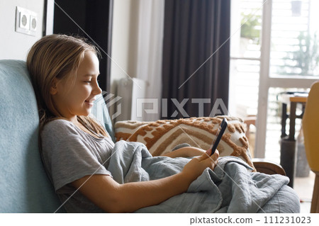 A little girl sitting on a couch looking at a cell phone at home 111231023