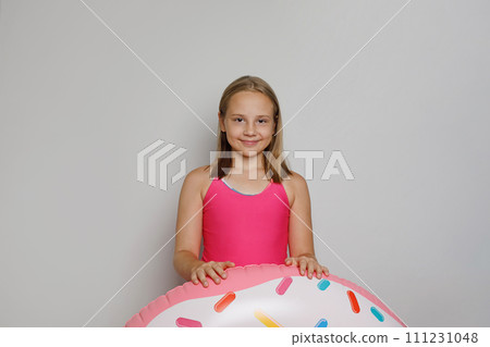 Cheerful child girl with pink rubber inflatable ring swimming pool float standing Cheerful child girl with pink rubber inflatable ring swimming pool float standing 111231048