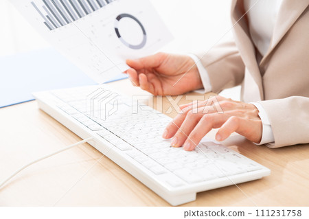 Hands of a middle-aged woman in a suit working at a desk with a computer 111231758