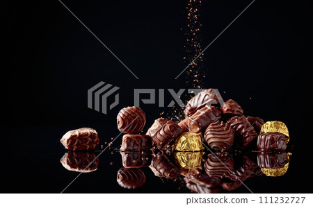 Various chocolate candies on a black background sprinkled with chocolate chips. Various chocolate candies on a black background sprinkled with chocolate chips. 111232727