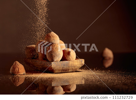 Chocolate truffles in small wooden dish sprinkled with cocoa powder. Black reflective background. Chocolate truffles in small wooden dish sprinkled with cocoa powder. Black reflective background. 111232729