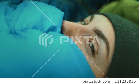 Person wake up in camping tent sleeping bag close up. Portrait of tourist girl opening eyes in cold morning. Female traveler vacation, trekking, hiking, tourism and outdoor activity. Side view 111232839