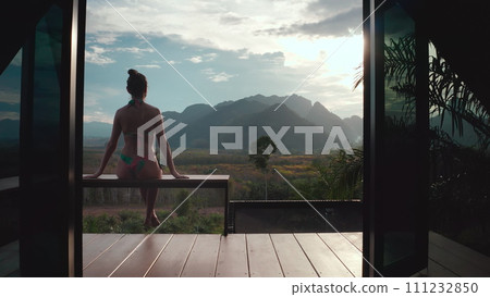 Woman enjoy tropical villa view sitting on terrace. Exotic lonely bungalow in jungles, mountains, forest, sunset. Female tourist on summer vacation. Travel holiday concept. Beautiful wild nature scene 111232850