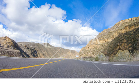 Vehicle is cruising along the Cuyama Highway under the bright sun. The surrounding landscape is illuminated by the radiant sunshine, creating a picturesque and inviting scene as the car travels 111233055