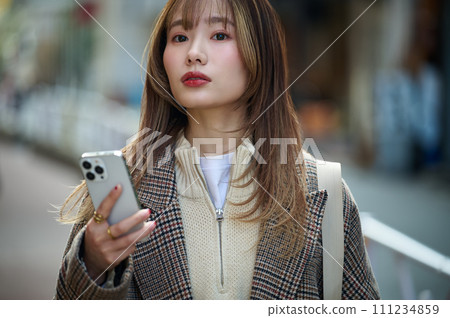 穿著冬衣的年輕女子拿著智慧型手機 穿著冬衣的年輕女子拿著智慧型手機 111234859