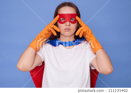 Tired sick Caucasian brown haired woman wearing superhero costume white T-shirt and rubber gloves isolated over blue background massaging painful temples felling headache Tired sick Caucasian brown haired woman wearing superhero costume white T-shirt and rubber gloves isolated over blue background massaging painful temples felling headache 111235402