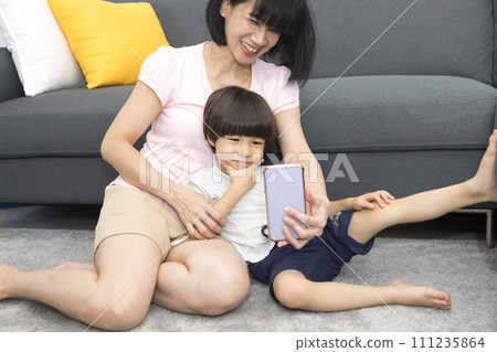 Family, technology and people concept - happy smiling mother and little son with smartphone having video call. 111235864