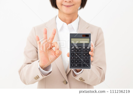 一位身穿米色西裝的中年女商人拿著黑色計算器,用手指做一個圓圈標誌 一位身穿米色西裝的中年女商人拿著黑色計算器,用手指做一個圓圈標誌 111236219