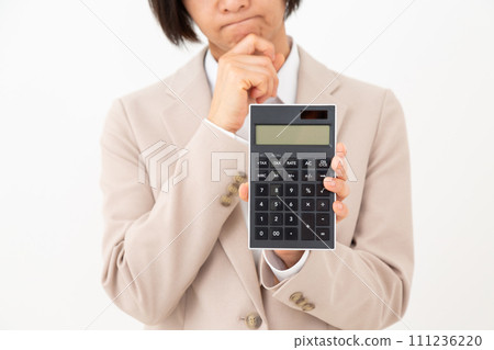 A middle-aged business woman wearing a beige suit holding a black calculator and worrying 111236220