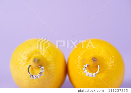 Intimate piercing. Minimal piercing concept. Two lemons with piercings on a lilac background Intimate piercing. Minimal piercing concept. Two lemons with piercings on a lilac background 111237255