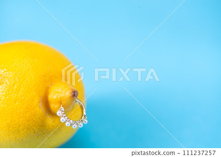 Intimate piercing. Minimal piercing concept. Lemon with piercing on blue background Intimate piercing. Minimal piercing concept. Lemon with piercing on blue background 111237257