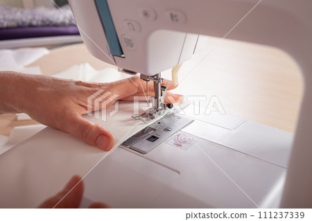 Seamstress at work. Dressmaker making clothes in modern studio. Tailor holding pencil and marking fabric. Woman standing at table with cut textile, sewing machine, thread, pins, needles, tape, cutouts Seamstress at work. Dressmaker making clothes in modern studio. Tailor holding pencil and marking fabric. Woman standing at table with cut textile, sewing machine, thread, pins, needles, tape, cutouts 111237339