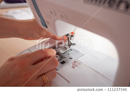 Seamstress at work. Dressmaker making clothes in modern studio. Tailor holding pencil and marking fabric. Woman standing at table with cut textile, sewing machine, thread, pins, needles, tape, cutouts Seamstress at work. Dressmaker making clothes in modern studio. Tailor holding pencil and marking fabric. Woman standing at table with cut textile, sewing machine, thread, pins, needles, tape, cutouts 111237340