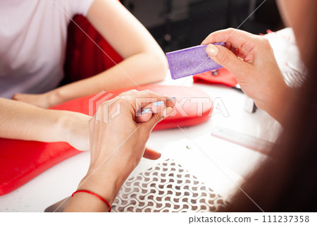 The manicurist holds hands of the client in beauty salon on desktop for manicure with nail polishes, napkins, creams and lighting instruments 111237358