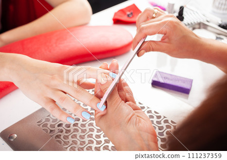 The manicurist holds hands of the client in beauty salon on desktop for manicure with nail polishes, napkins, creams and lighting instruments The manicurist holds hands of the client in beauty salon on desktop for manicure with nail polishes, napkins, creams and lighting instruments 111237359