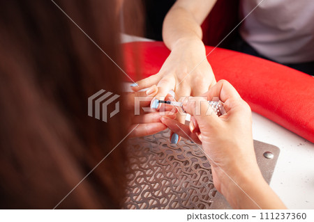 The manicurist holds hands of the client in beauty salon on desktop for manicure with nail polishes, napkins, creams and lighting instruments The manicurist holds hands of the client in beauty salon on desktop for manicure with nail polishes, napkins, creams and lighting instruments 111237360