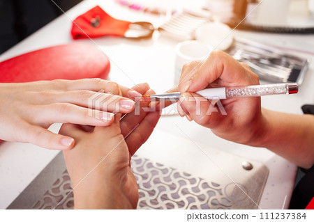 The manicurist holds hands of the client in beauty salon on desktop for manicure with nail polishes, napkins, creams and lighting instruments The manicurist holds hands of the client in beauty salon on desktop for manicure with nail polishes, napkins, creams and lighting instruments 111237384