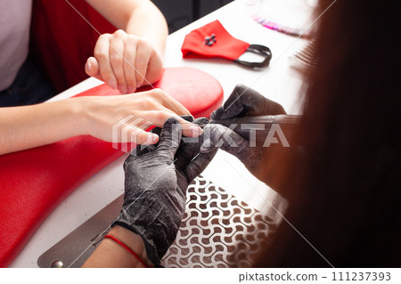 The manicurist holds hands of the client in beauty salon on desktop for manicure with nail polishes, napkins, creams and lighting instruments The manicurist holds hands of the client in beauty salon on desktop for manicure with nail polishes, napkins, creams and lighting instruments 111237393
