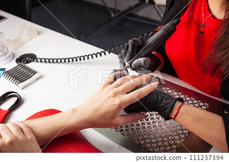 The manicurist holds hands of the client in beauty salon on desktop for manicure with nail polishes, napkins, creams and lighting instruments 111237394
