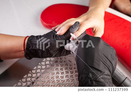 The manicurist holds hands of the client in beauty salon on desktop for manicure with nail polishes, napkins, creams and lighting instruments The manicurist holds hands of the client in beauty salon on desktop for manicure with nail polishes, napkins, creams and lighting instruments 111237399