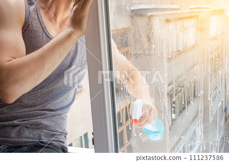 A man washes a window from the outside. The man sprays a blue cleaner A man washes a window from the outside. The man sprays a blue cleaner 111237586