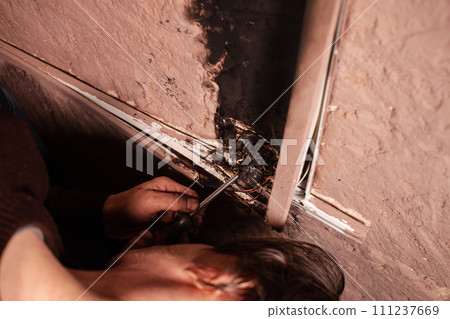 A man fixes a burnt socket. Short circuit, burnt wires. traces of smoke fire on the wall. The electrical outlet was completely melted, the voltage drop from the use of an electric heater. Screwdriver 111237669
