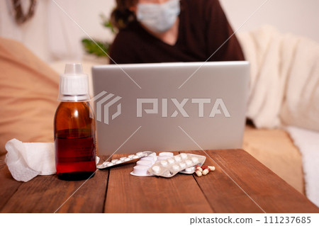 A sick man in a medical mask against the background of tablets. Home quarantine, coronavirus, A man lies on a bed with a laptop. A sick man in a medical mask against the background of tablets. Home quarantine, coronavirus, A man lies on a bed with a laptop. 111237685