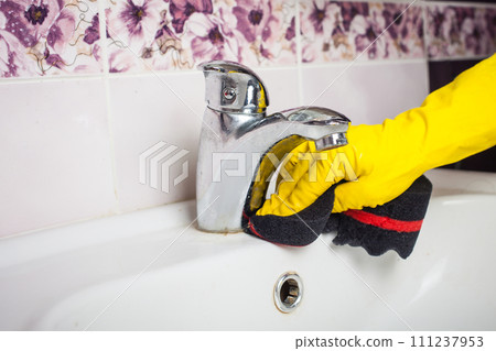 Maid with rubber glove cleaning tap and sink. 111237953